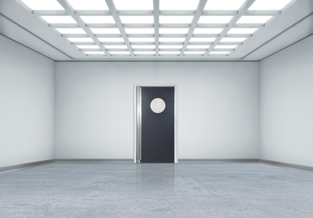 Minimalist white room with grid lights and a black door with round window.
