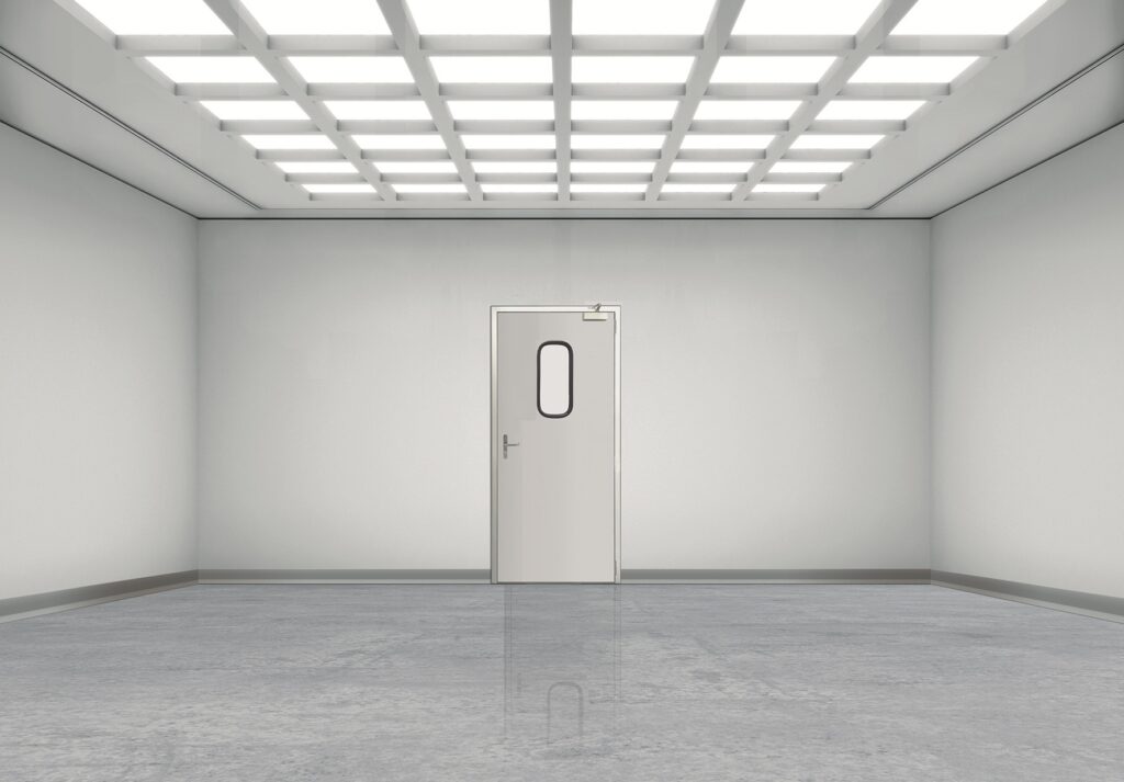 Empty white room with grid-lit ceiling and a centered door with oval window