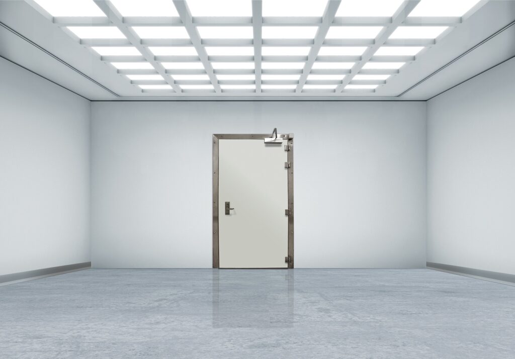 Empty white room with a metal-framed door and bright grid ceiling lights.