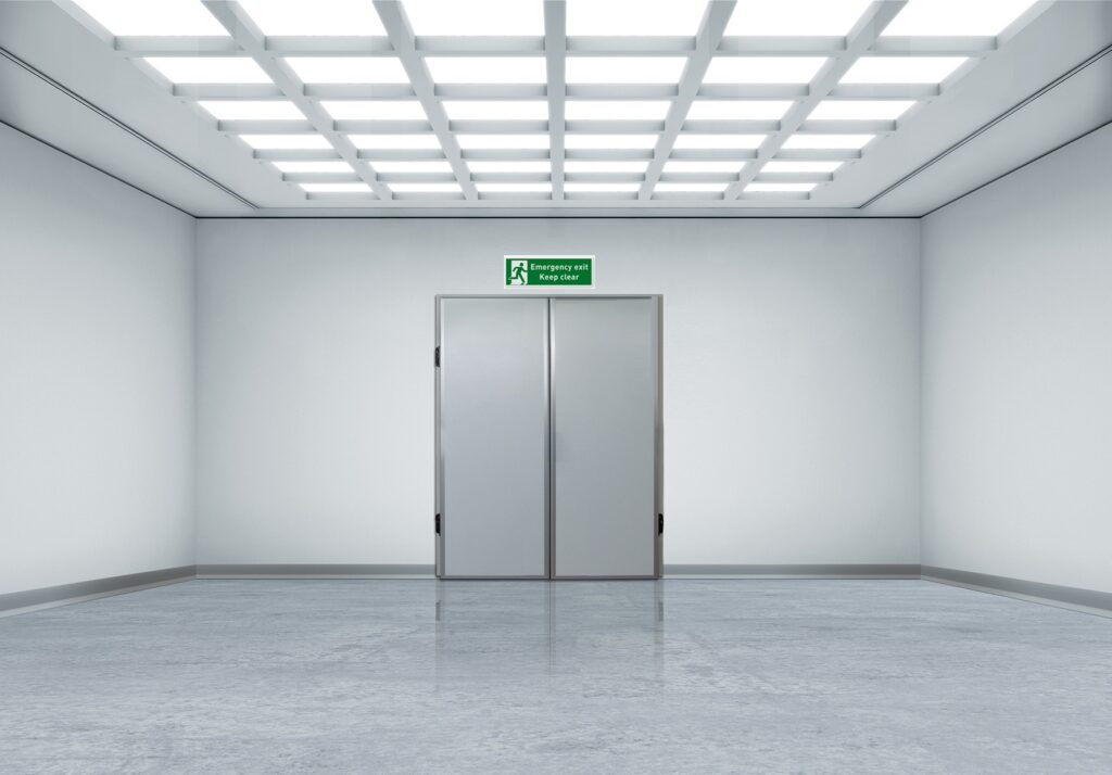 Bright empty corridor with double doors and a green emergency exit sign.